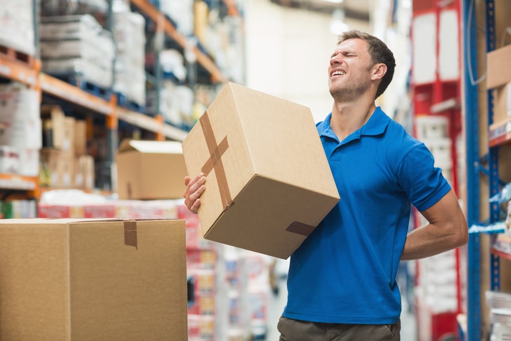 Side view of worker with backache while lifting box in the warehouse